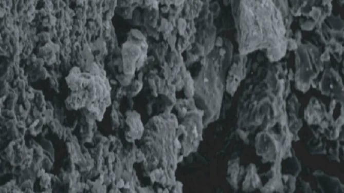 Grayscale microscopic view of rough, crystalline or granular surface texture with irregular bumpy formations
