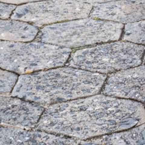 Close-up of irregular gray stone or slate tiles with moss between cracks and mortar joints